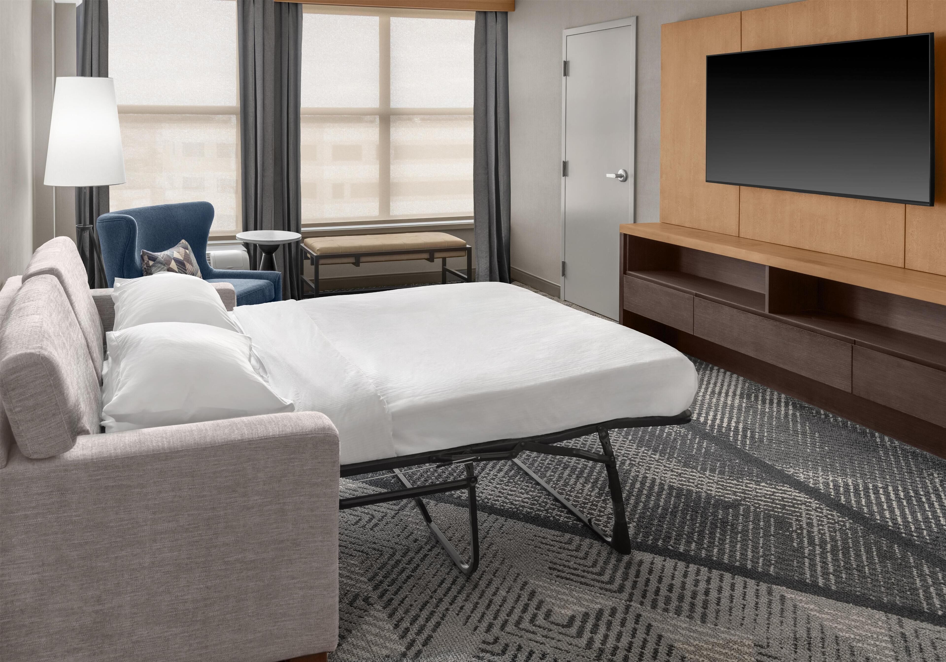 Ein Hotelzimmer mit Bett, Sofa, Sessel, kleinem Tisch, Fernseher und einer Tür.