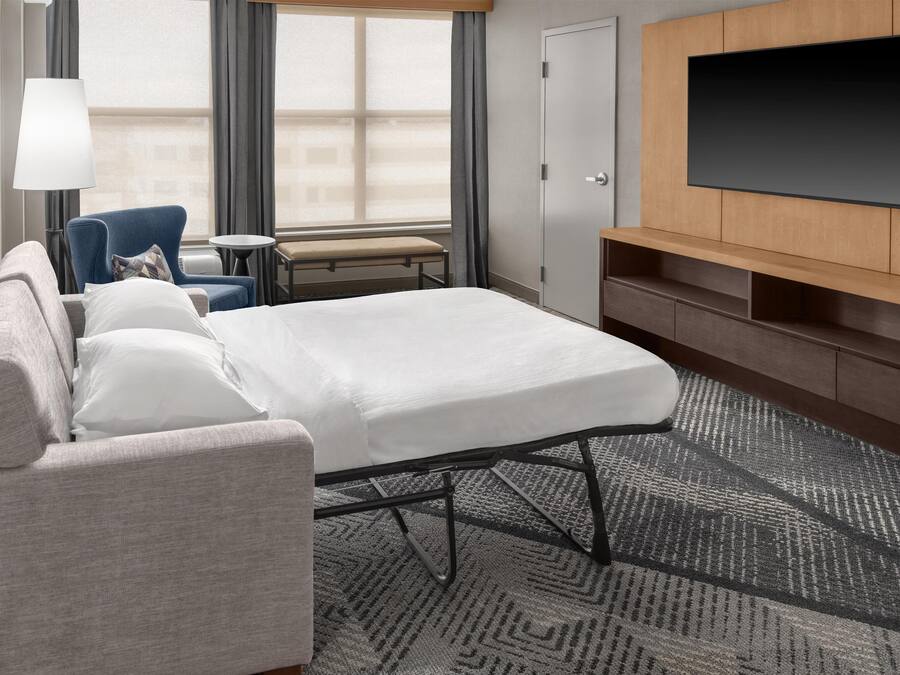 Ein Hotelzimmer mit Bett, Sofa, Sessel, kleinem Tisch, Fernseher und einer Tür.