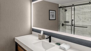 A modern bathroom with a large mirror, a sink, a towel, and a shower area. - DoubleTree by Hilton Dayton Fairborn (Fairborn)