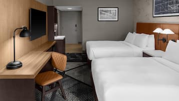 A hotel room with a desk, two beds, a chair, a TV, and a framed picture on the wall.