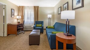 A hotel room with a desk, two chairs, a sofa, a round table, and a standing lamp. - Comfort Inn & Suites - near Robins Air Force Base Main Gate (Warner Robins)