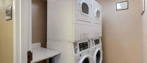 A laundry room with stacked washers and dryers, a control panel, and a small shelf.
