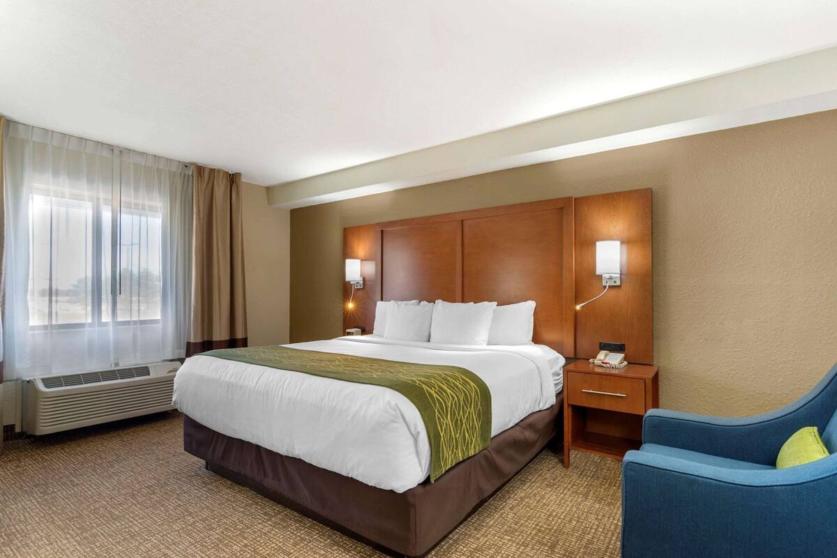 A hotel room with a bed, a chair, a nightstand, a lamp, and a window with curtains.