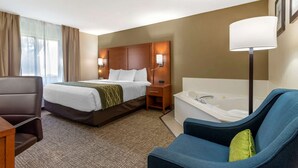 A hotel room with a bed, a desk, a chair, a bathtub, and a window with curtains. - Comfort Inn & Suites - near Robins Air Force Base Main Gate (Warner Robins)