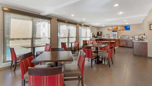 A spacious dining area with multiple tables and chairs, large windows, and a kitchen area with a counter and appliances. - Comfort Inn & Suites - near Robins Air Force Base Main Gate (Warner Robins)