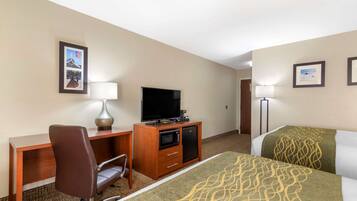 A hotel room with a bed, a desk with a chair, a television, a microwave, and a lamp.