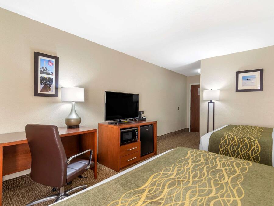 A hotel room with a bed, a desk with a chair, a television, a microwave, and a lamp.