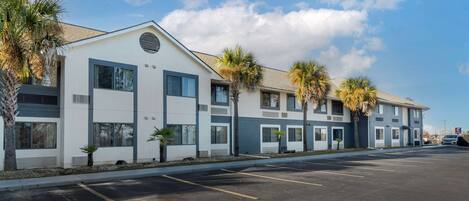 A modern hotel with a row of rooms, a parking lot, and palm trees.