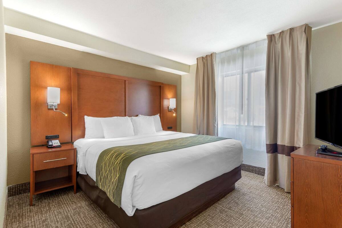 A hotel room with a large bed, bedside tables, a TV, and a window with curtains.