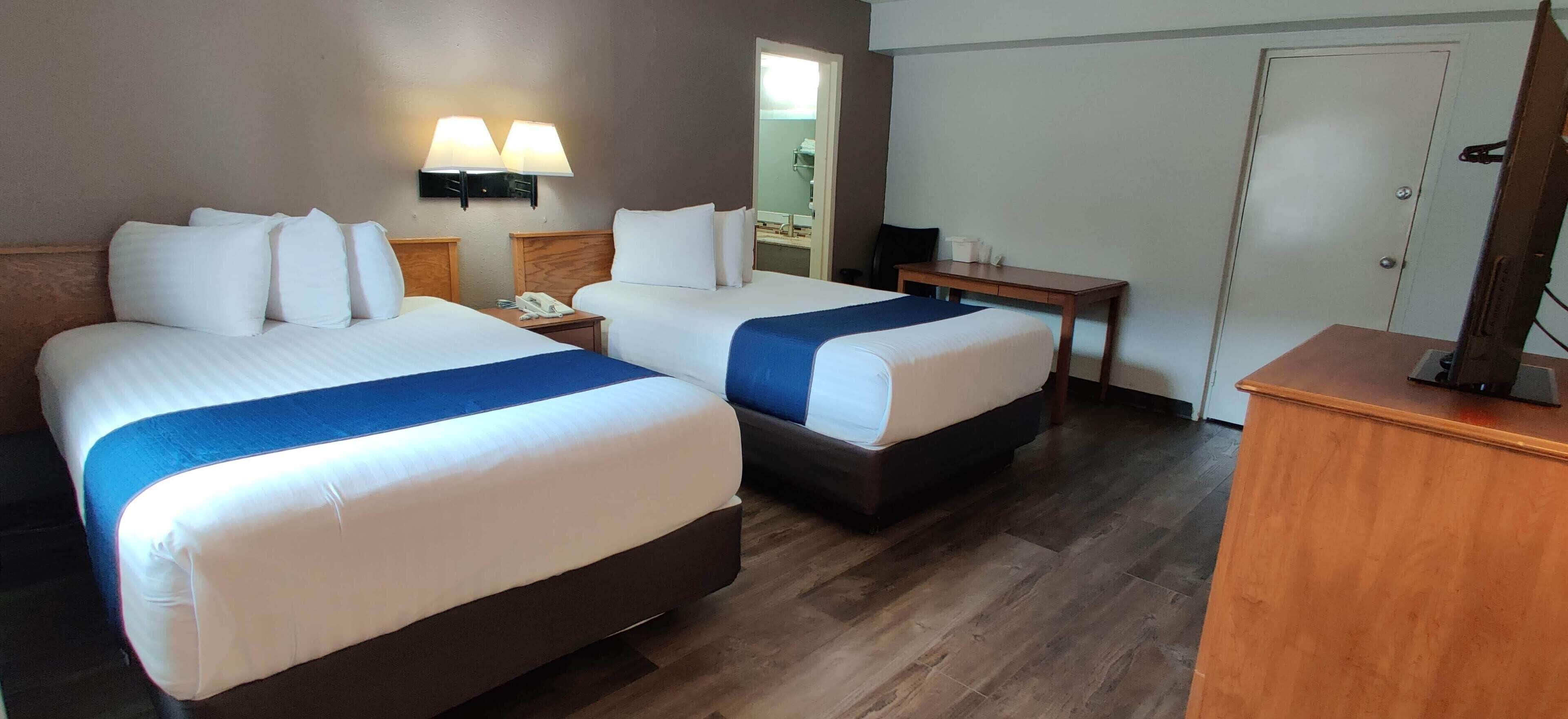 Habitación de hotel con dos camas, un escritorio, un espejo y una televisión.