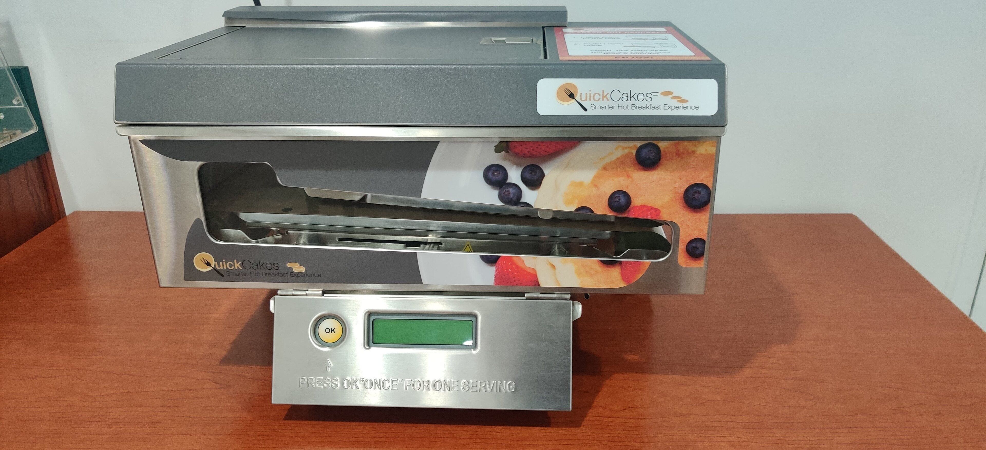 A Quick Cakes breakfast machine with a digital display and a push button.