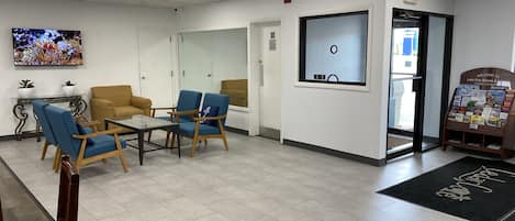 A reception area with a reception desk, two blue chairs, a yellow sofa, a television, and a welcome sign.
