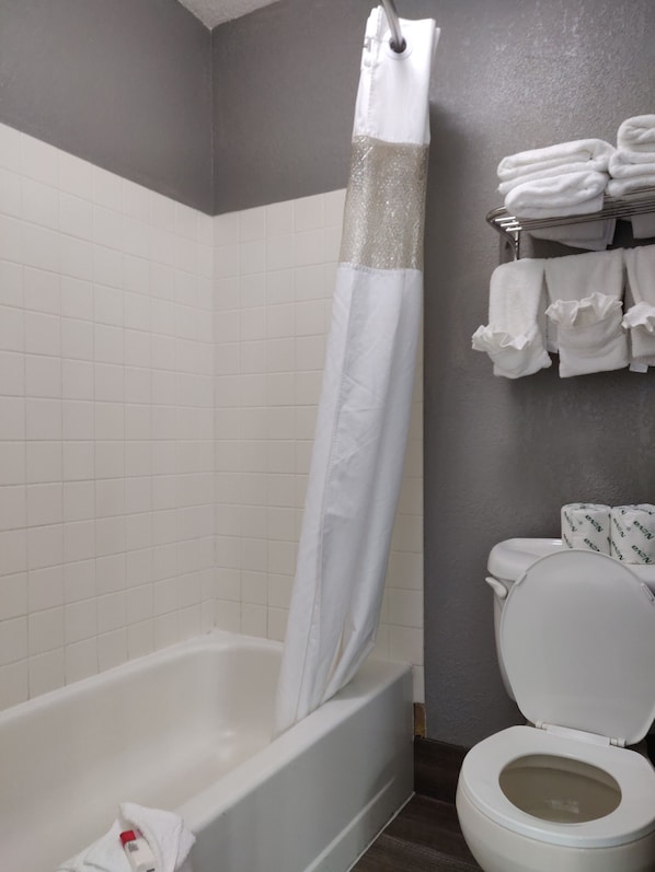 A bathroom with a bathtub, a shower curtain, a toilet, and a towel rack with folded towels.