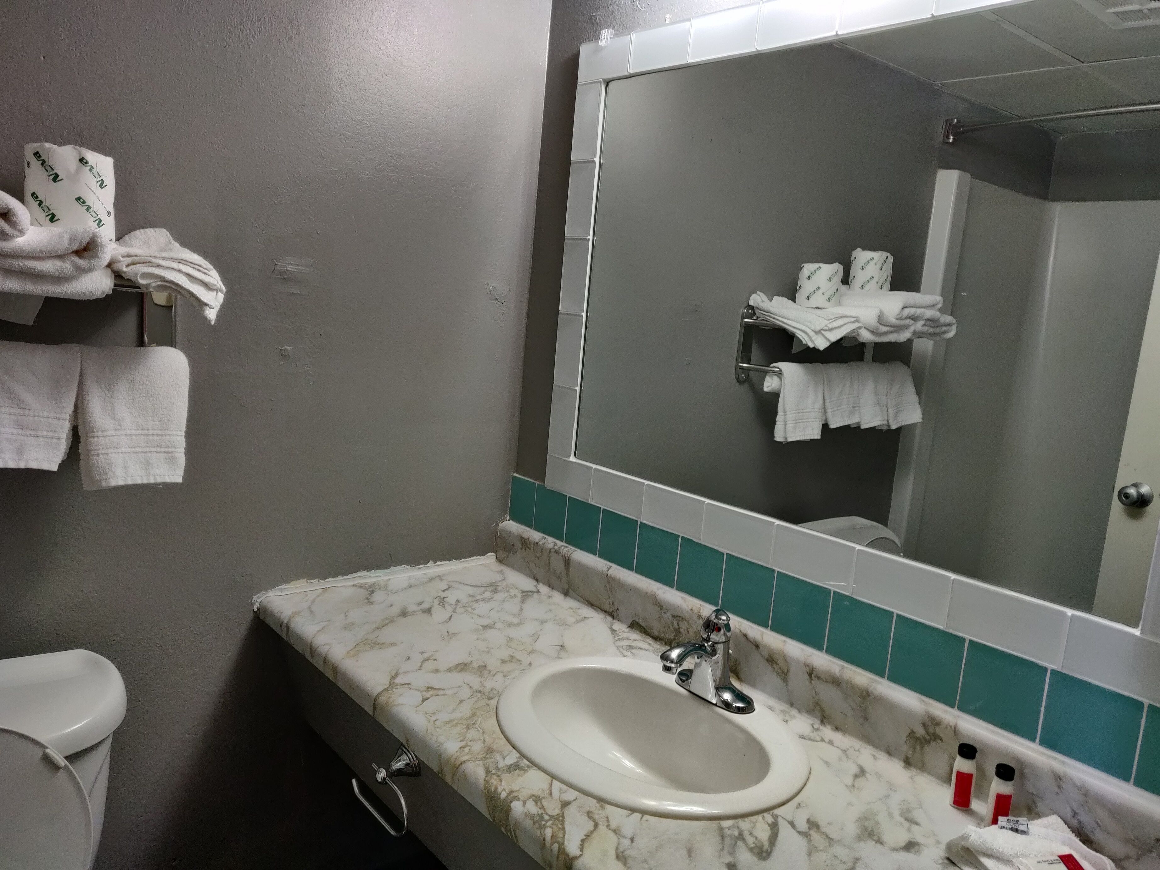 A bathroom with a marble sink, a mirror, and towels on a rack.