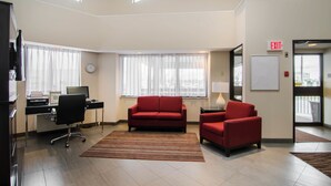 Habitación de hotel moderna con escritorio, computadora, sofá rojo y vistas a la ciudad a través de amplias ventanas.