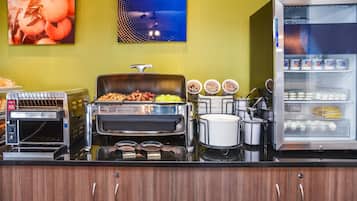 Montaje tipo bufé con una variedad de alimentos, que incluye una parrilla, un refrigerador con bebidas y una presentación de frutas.