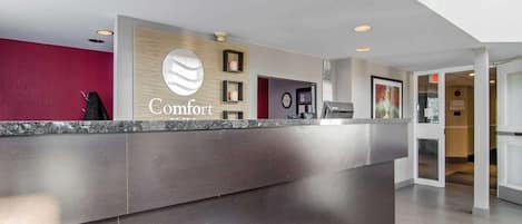 Zona de recepción de un hotel con diseño moderno, que incluye un mostrador de recepción, un reloj y un letrero en la pared que dice "Comfort".