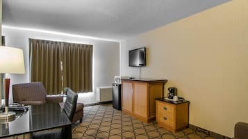 A hotel room with a dining table, two chairs, a television, a small cabinet, and a patterned carpet.