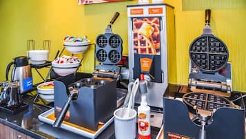 Una estación de gofres con varias planchas para gofres, una máquina para hacer gofres y un dispensador de masa para gofres.