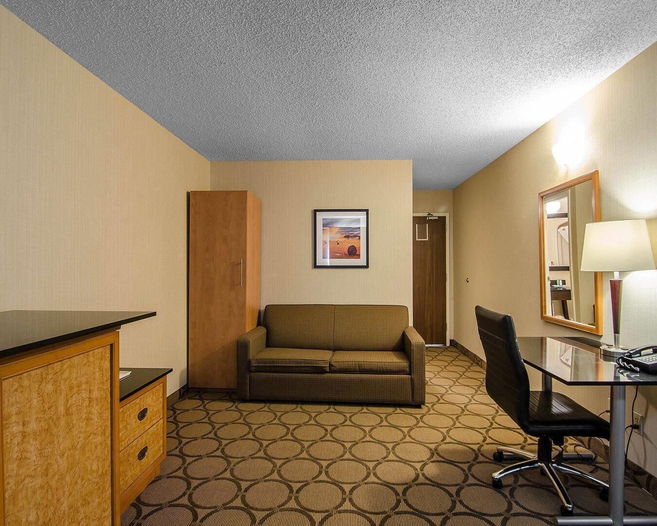 A hotel room with a sofa, a desk with a chair, a mirror, and a framed picture on the wall.