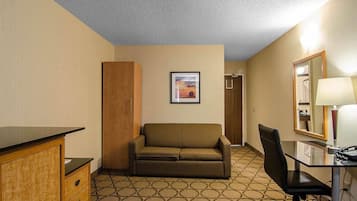 A hotel room with a sofa, a desk with a chair, a mirror, and a framed picture on the wall.