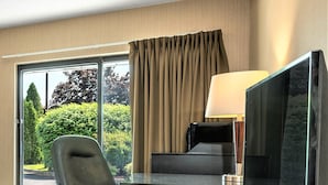 Habitación de hotel con escritorio, silla, televisor y ventanas amplias con cortinas.