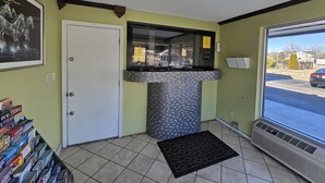 A reception area with a tiled floor, a door, a window with a view of the street, a wall-mounted air conditioner, and a display of board games. - Sunrise Inn By OYO Newport News US-60 (Newport News)