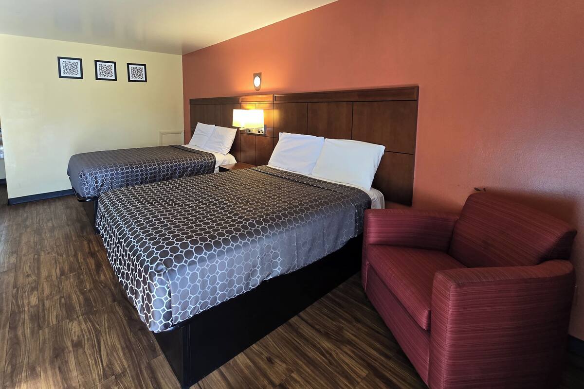 A hotel room with two beds, a red armchair, and a wooden floor.