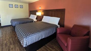 A hotel room with two beds, a red armchair, and a wooden floor.