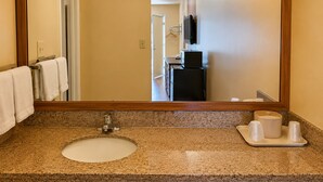 A bathroom with a granite countertop, a sink, a mirror, a towel rack, a black refrigerator, and a television mounted on the wall. - Sunrise Inn By OYO Newport News US-60 (Newport News)