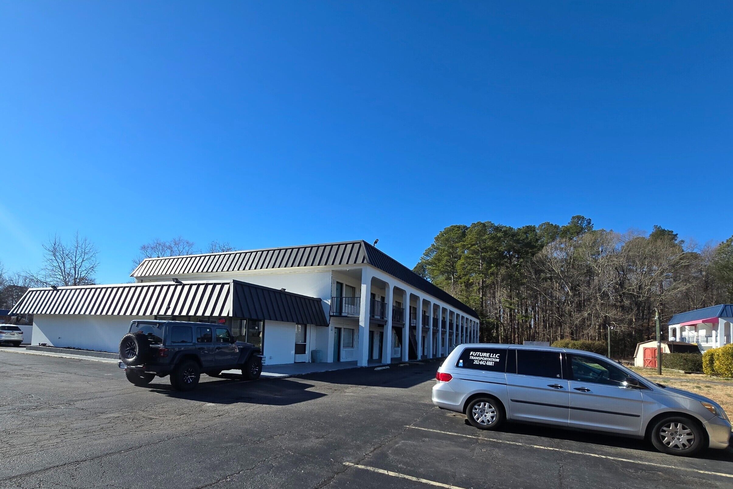 A building with a white exterior and a black roof, featuring a covered parking area with two vehicles parked.