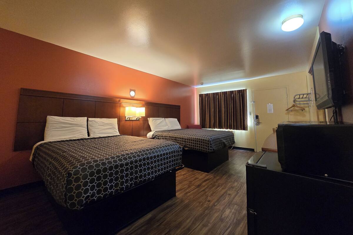 A hotel room with two beds, a TV, and a desk.