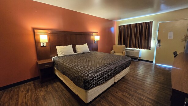 A hotel room with a large bed, two bedside tables with lamps, a chair, and a window with curtains. - Sunrise Inn By OYO Newport News US-60 (Newport News)