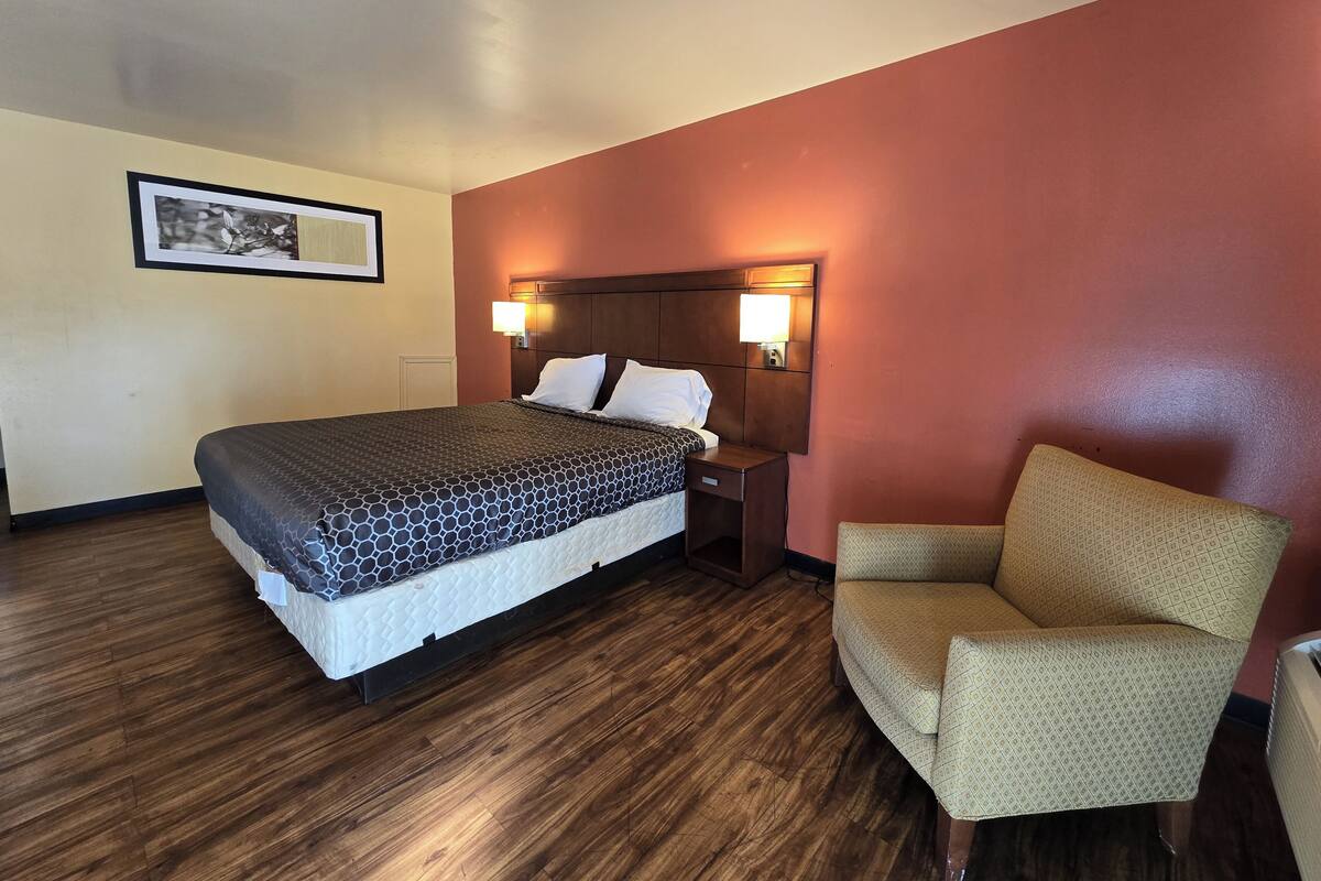 A hotel room with a bed, a nightstand, a chair, and a framed picture on the wall.