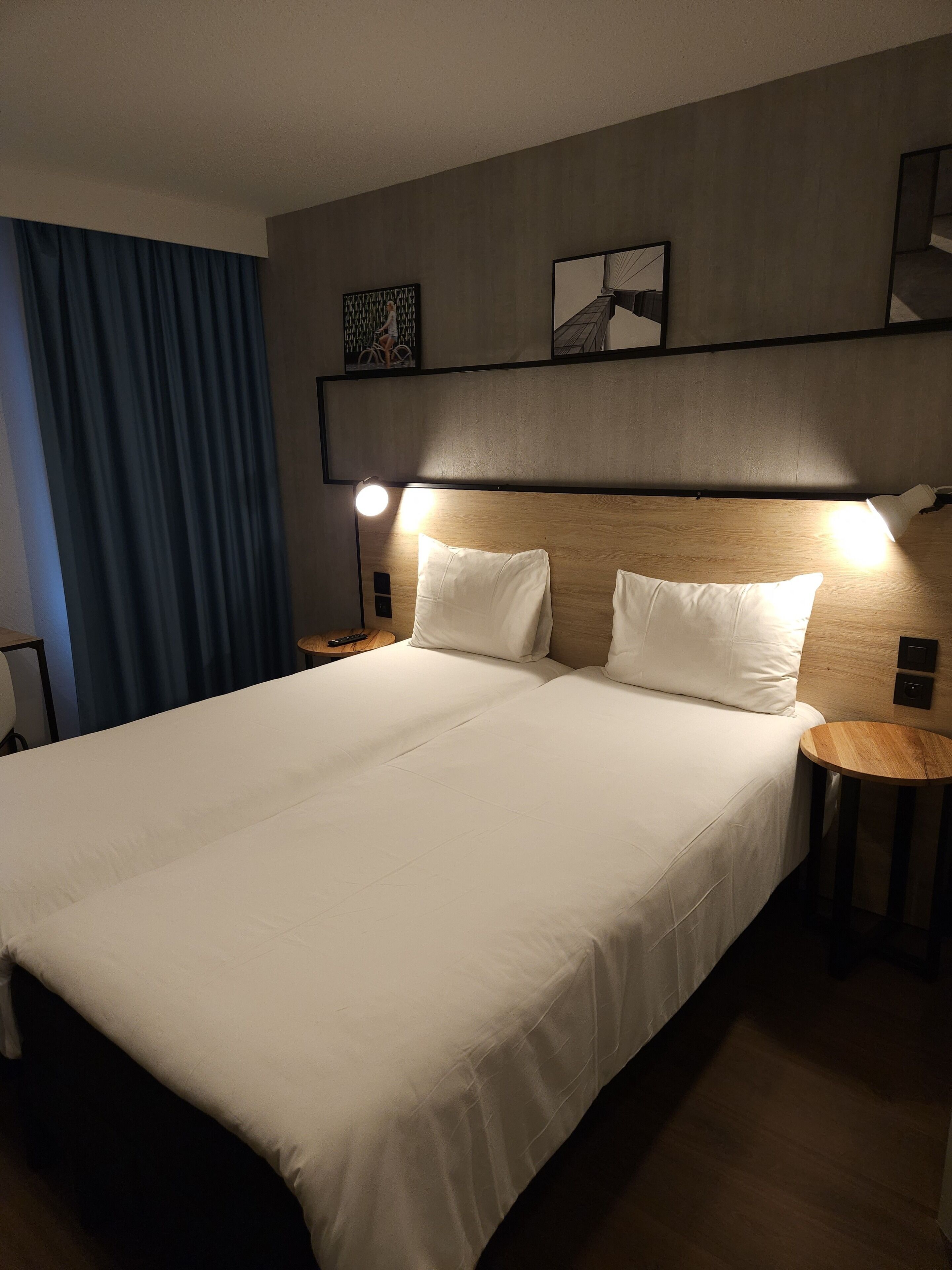 Habitación de hotel con una cama grande, dos mesitas de noche, un cabecero y una cortina azul.