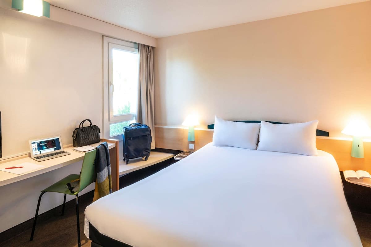 Ein Hotelzimmer mit Bett, Schreibtisch, Stuhl, Laptop, Handtasche und Koffer.