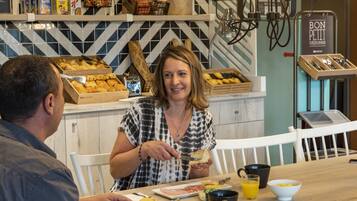Desayuno con una mujer cortando tostadas, un hombre comiendo y diversos alimentos sobre la mesa.