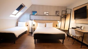 Habitación de hotel moderna con dos camas individuales, un escritorio con silla, televisor montado en la pared y un tragaluz.
