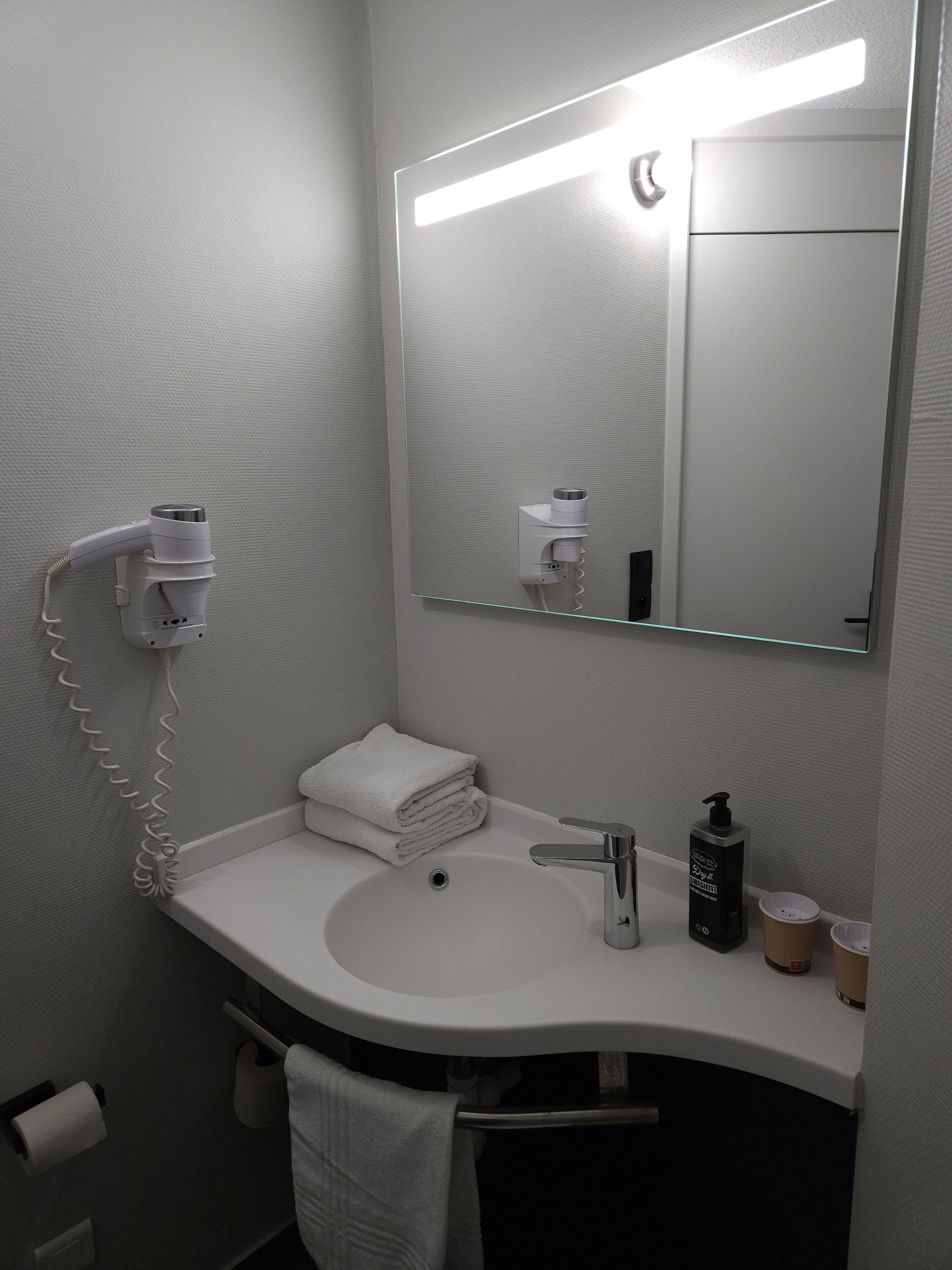A bathroom with a white sink, a mirror, a hairdryer, a towel, and a bottle of hand soap.