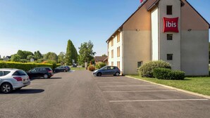 Un hotel de diseño moderno, con un llamativo logotipo rojo y blanco, un estacionamiento con varios coches y un césped bien cuidado.