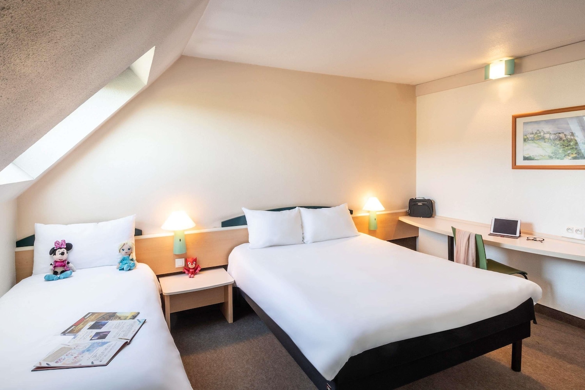 Habitación de hotel con dos camas, un escritorio, una computadora portátil y un cuadro en la pared.