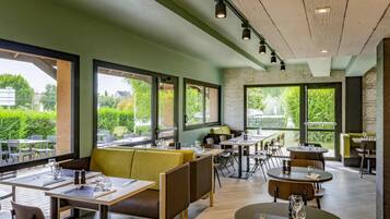 Un restaurante con mesas en el interior, amplias ventanas y vistas a zonas verdes.