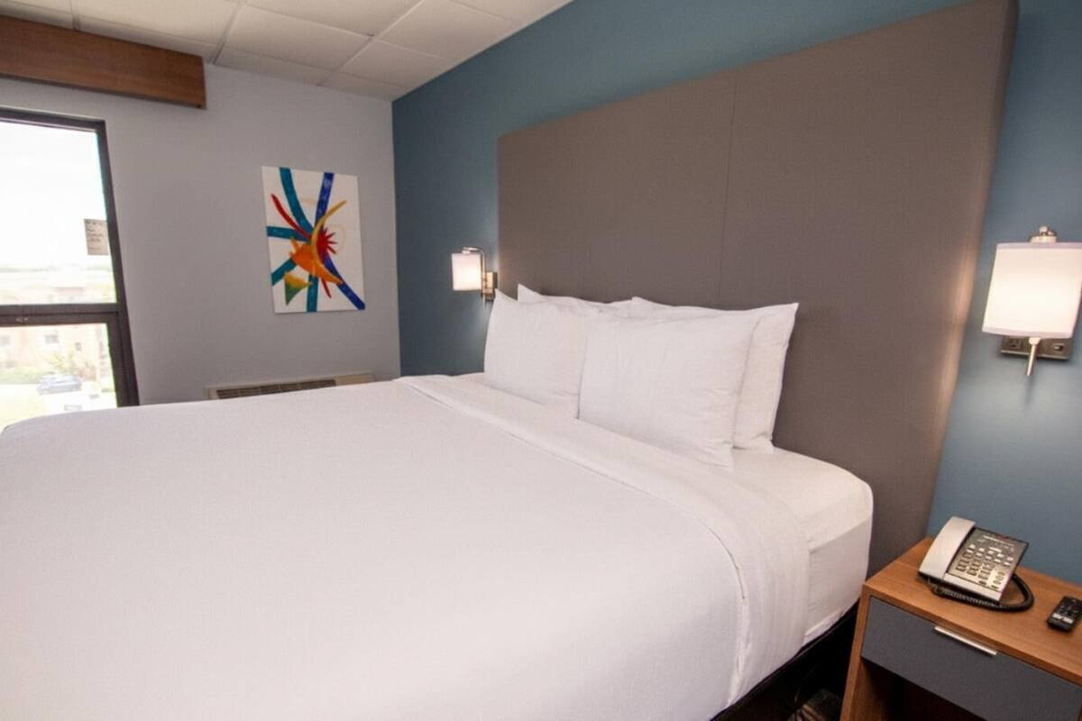 Ein Hotelzimmer mit einem großen Bett, einem Nachttisch mit Telefon und einer Wandleuchte.
