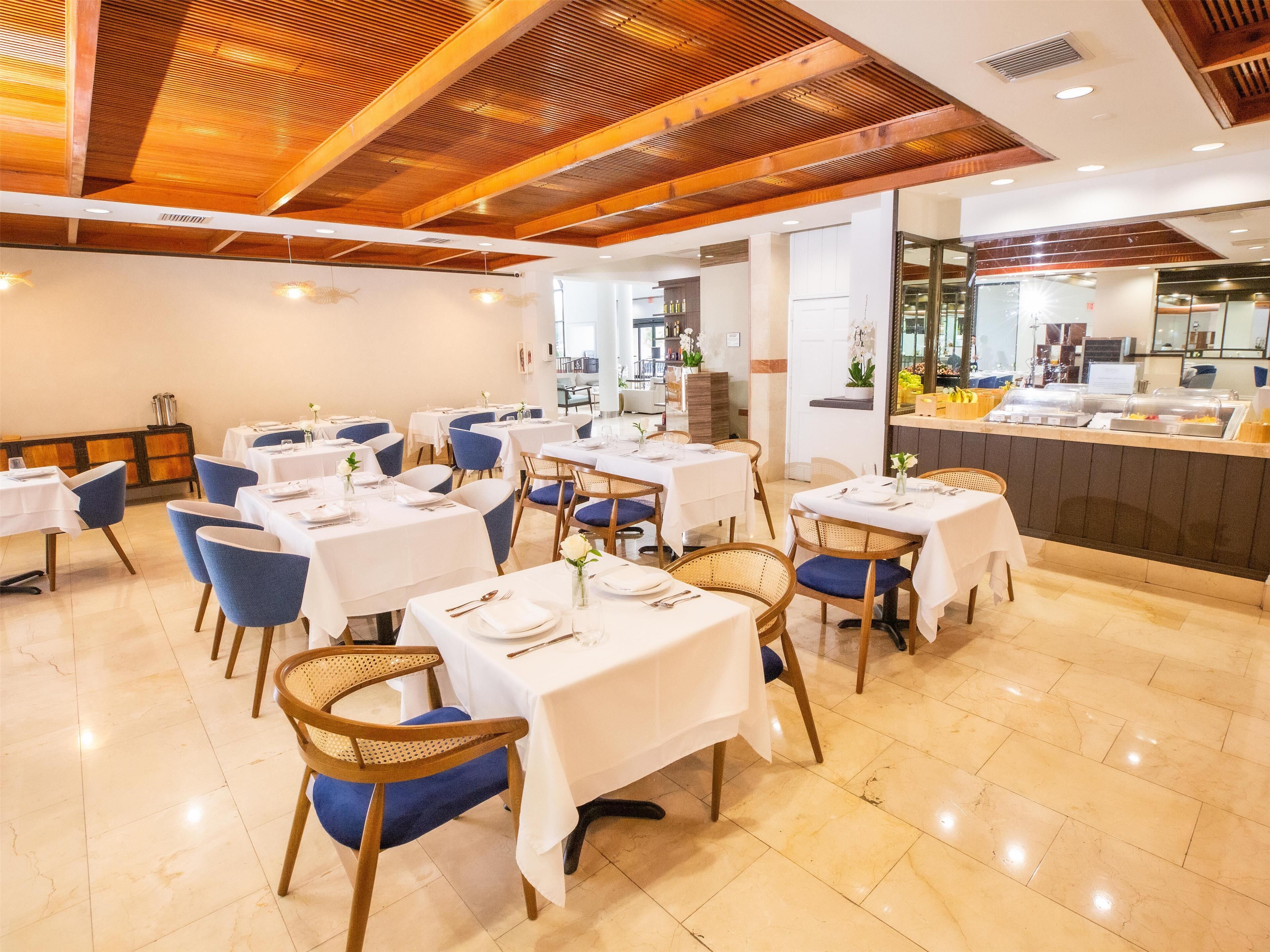 Um restaurante com toalhas de mesa brancas, cadeiras azuis e teto de madeira.