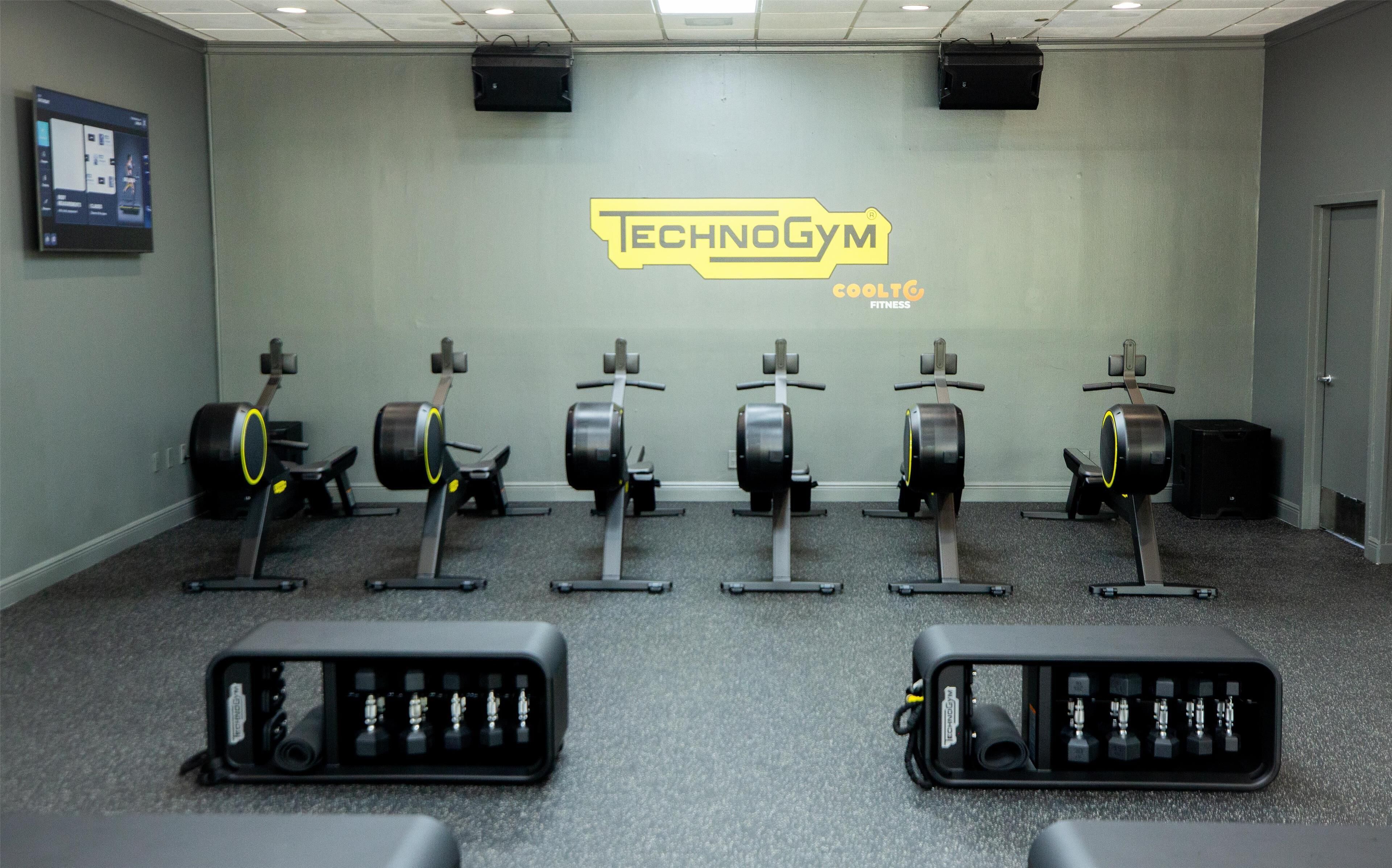 Una palestra con attrezzature per esercizi cardio, uno schermo a parete e una porta sulla destra.