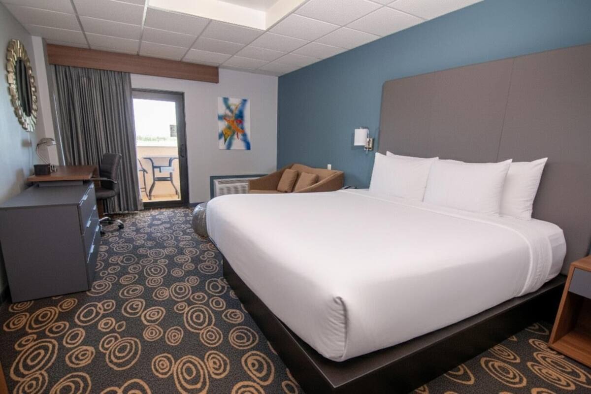 Ein Hotelzimmer mit einem großen Bett, einem Schreibtisch, einem Stuhl, einem kleinen Tisch und Blick ins Freie.