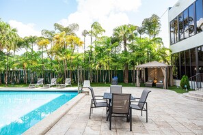 A poolside area with a pool, lounge chairs, and a covered seating area surrounded by lush greenery. - Regency Miami Airport by Sonesta (Miami)