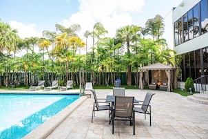 A poolside area with a pool, lounge chairs, and a covered seating area surrounded by lush greenery.