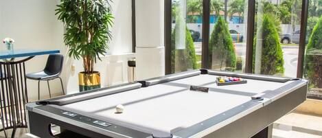 A pool table in a room with large windows, a potted plant, and a chair.