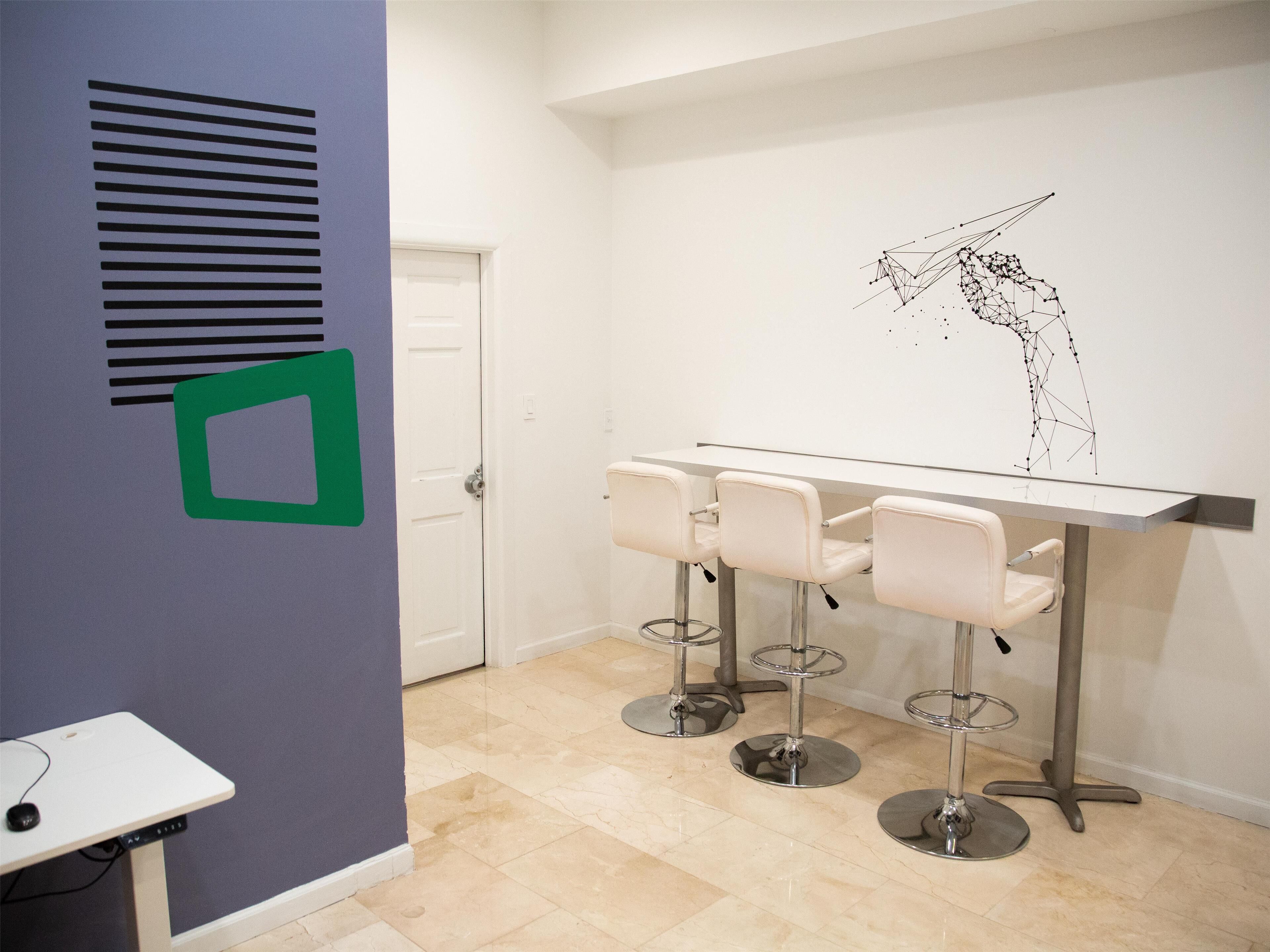 A modern kitchen with a white countertop, three bar stools, and a decorative wall art piece.